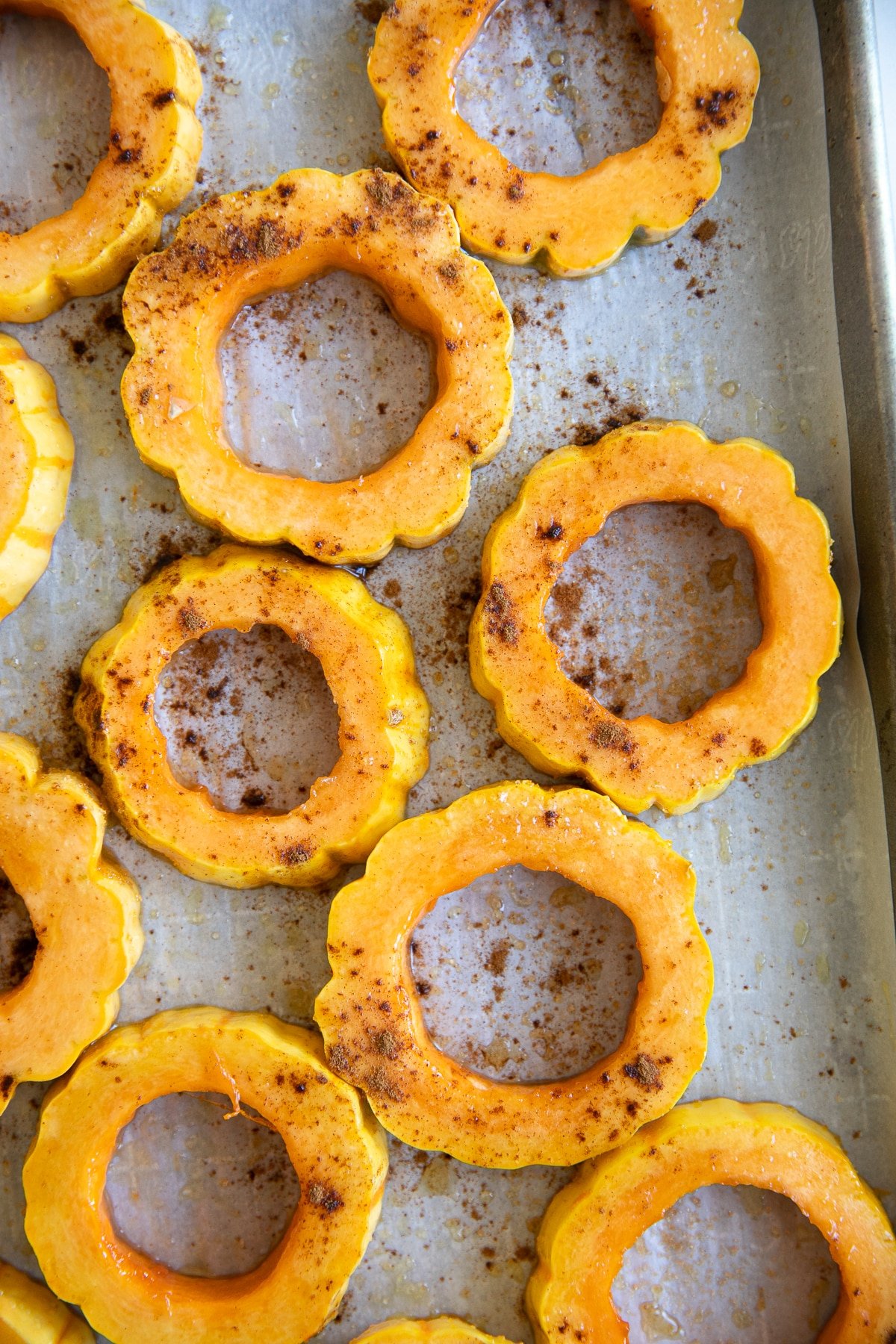 Sliced rings of delicata squash on a large baking sheet brushed with olive oil and sprinkled with ground cinnamon.