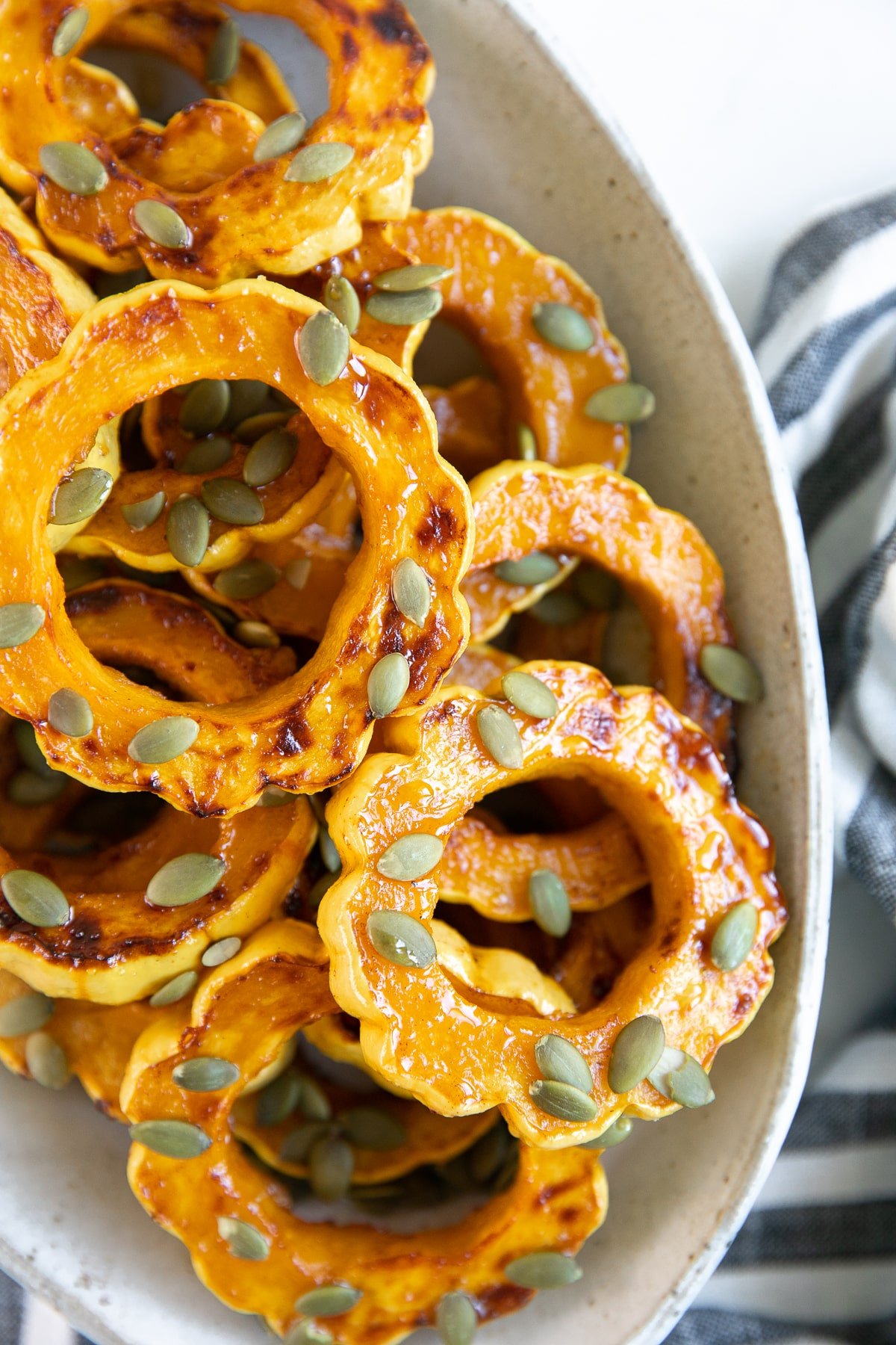 White platter filled with roasted delicata squash rings roasted in maple syrup, cinnamon, and sprinkled with pepitas.