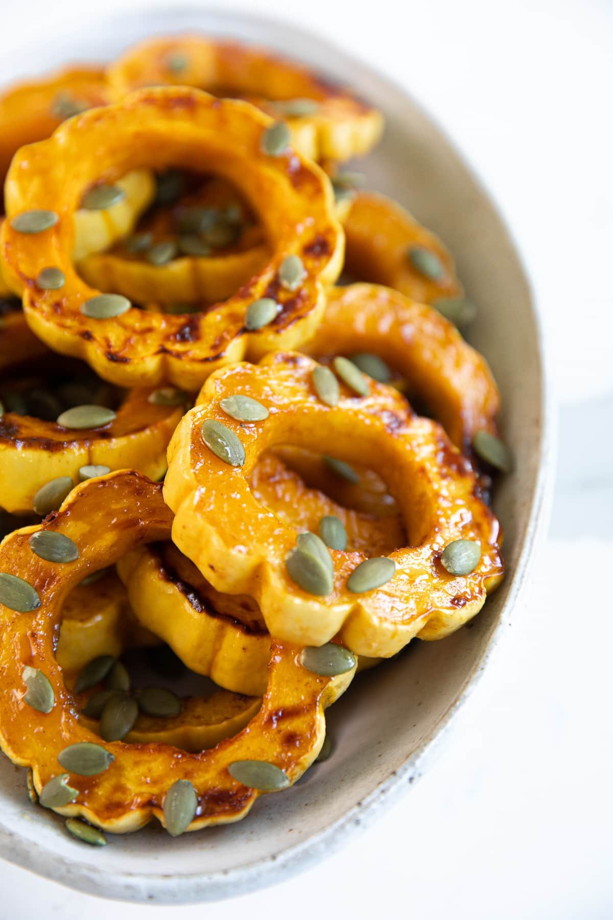 White platter filled with roasted delicata squash rings roasted in maple syrup, cinnamon, and sprinkled with pepitas.
