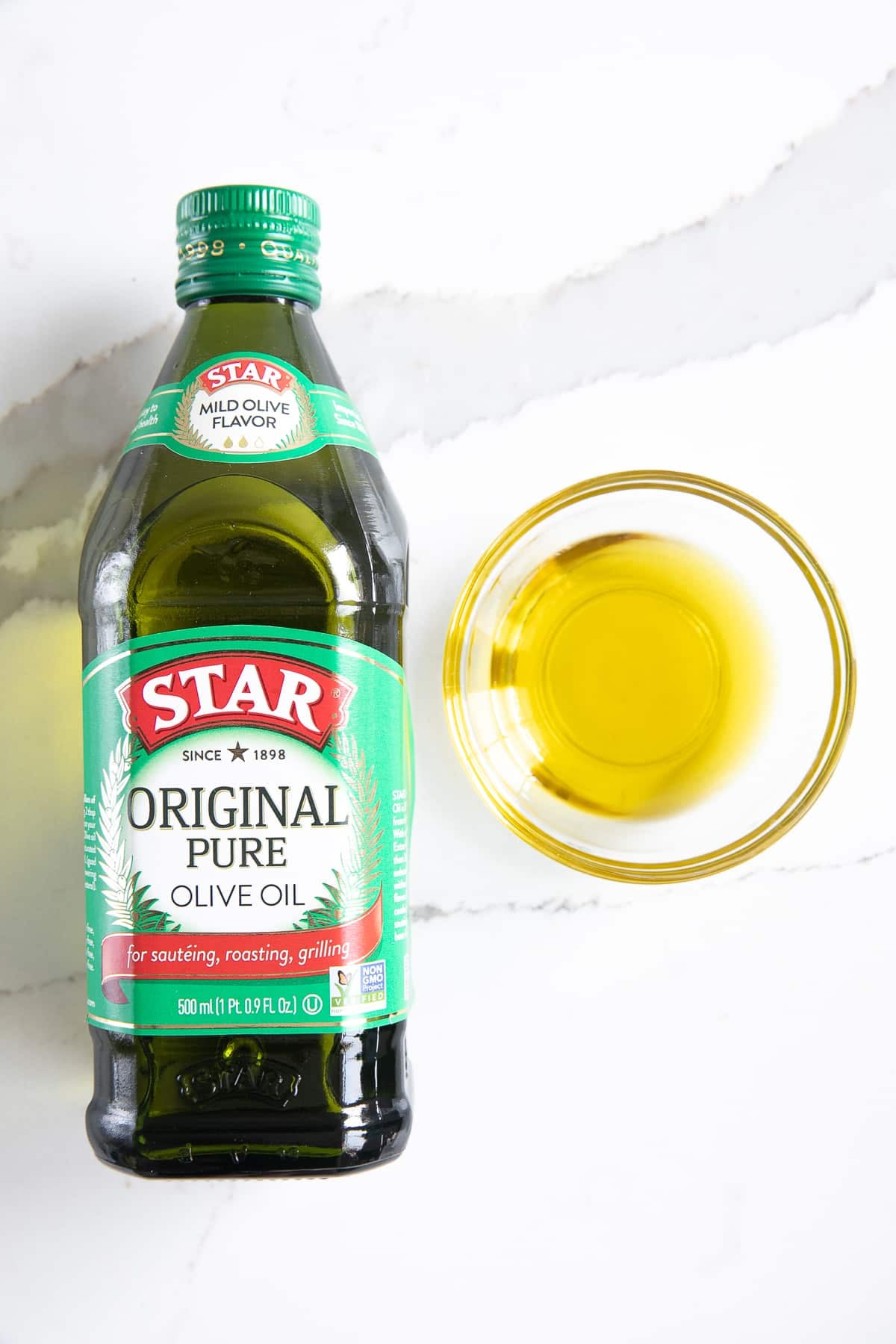 Bottle of pure olive oil with a small sample in a glass dish to its left