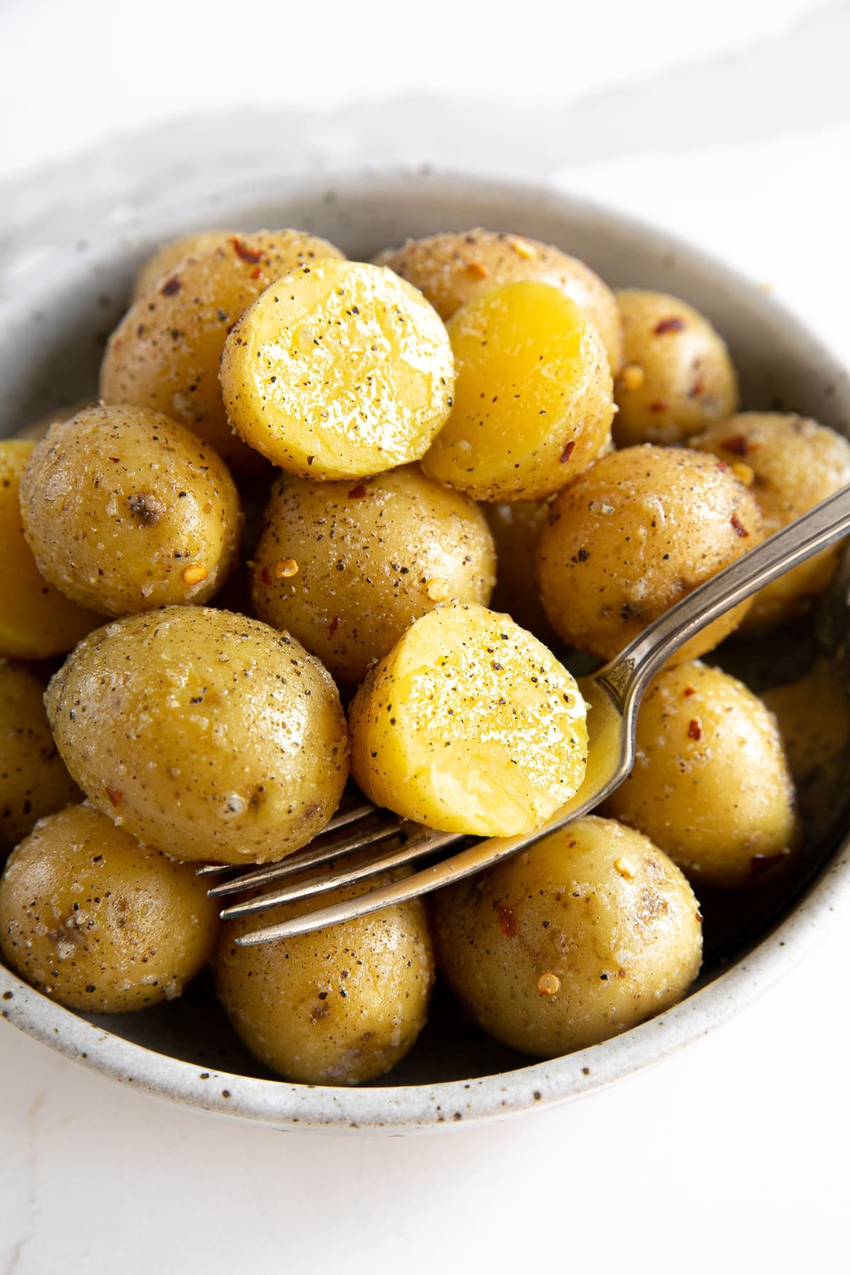 Round serving bowl filled with small yellow boiled potatoes coated in garlic and butter.