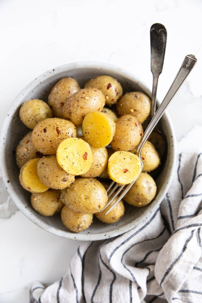 Round serving bowl filled with small yellow boiled potatoes coated in garlic, butter, and sprinkled with red chili flakes.