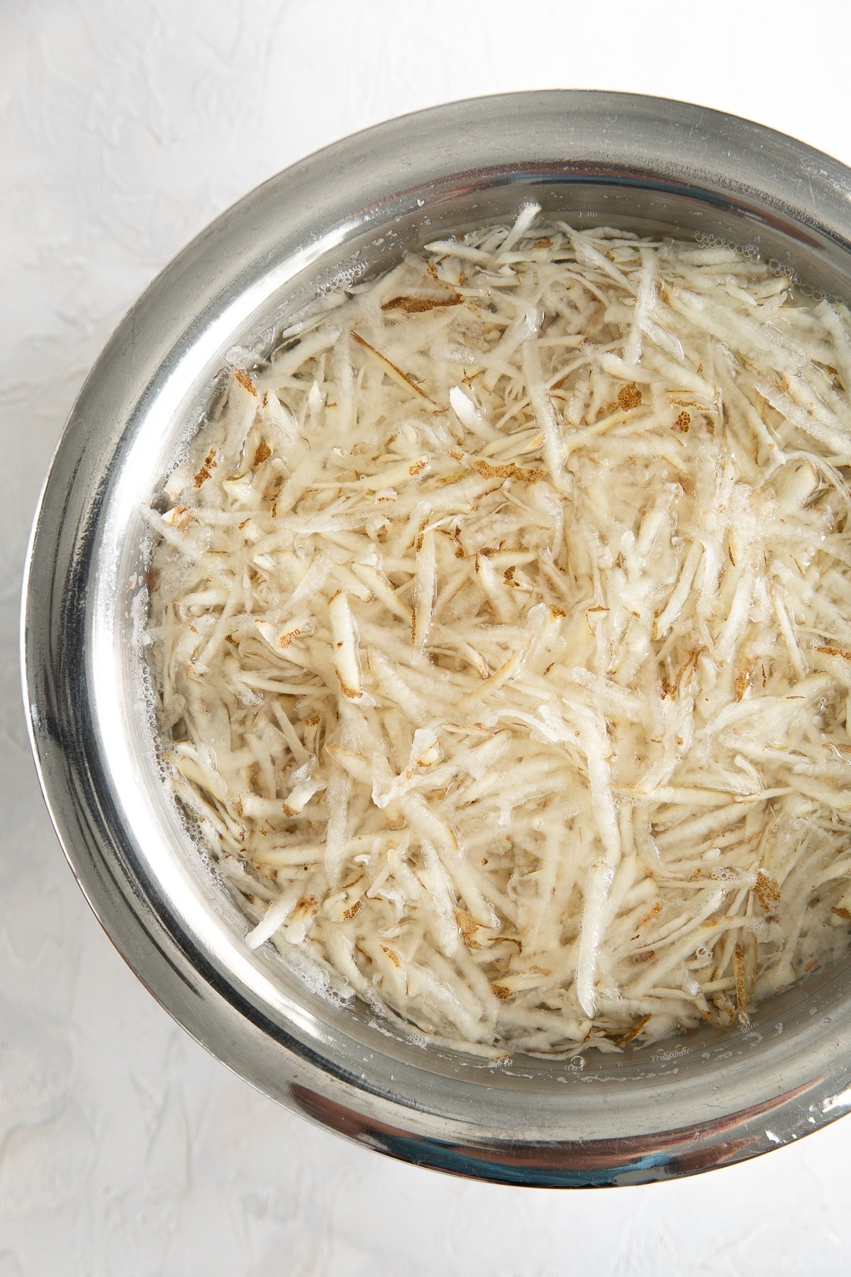 Shredded potatoes in a large bowl of cold water.
