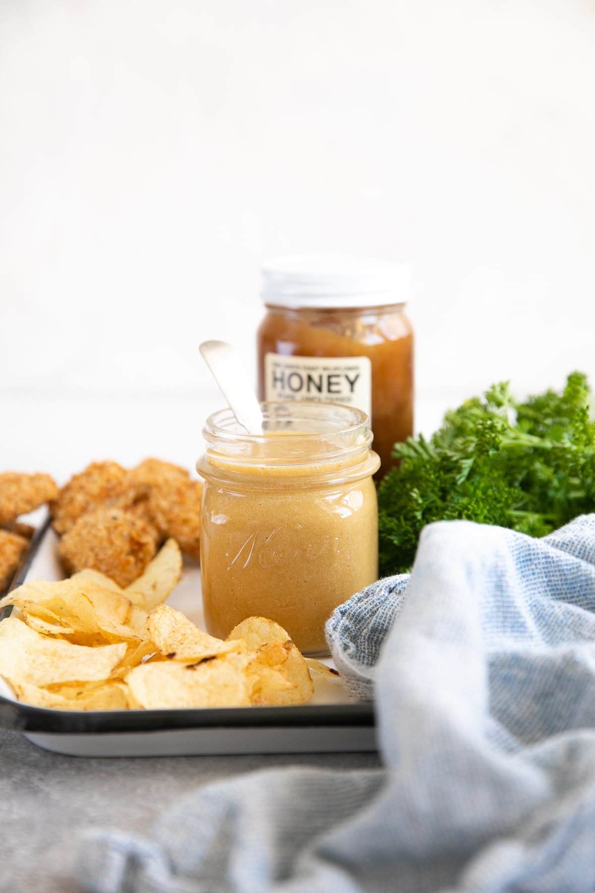 Easy honey mustard sauce in a small glass jar served with chips and chicken nuggets.