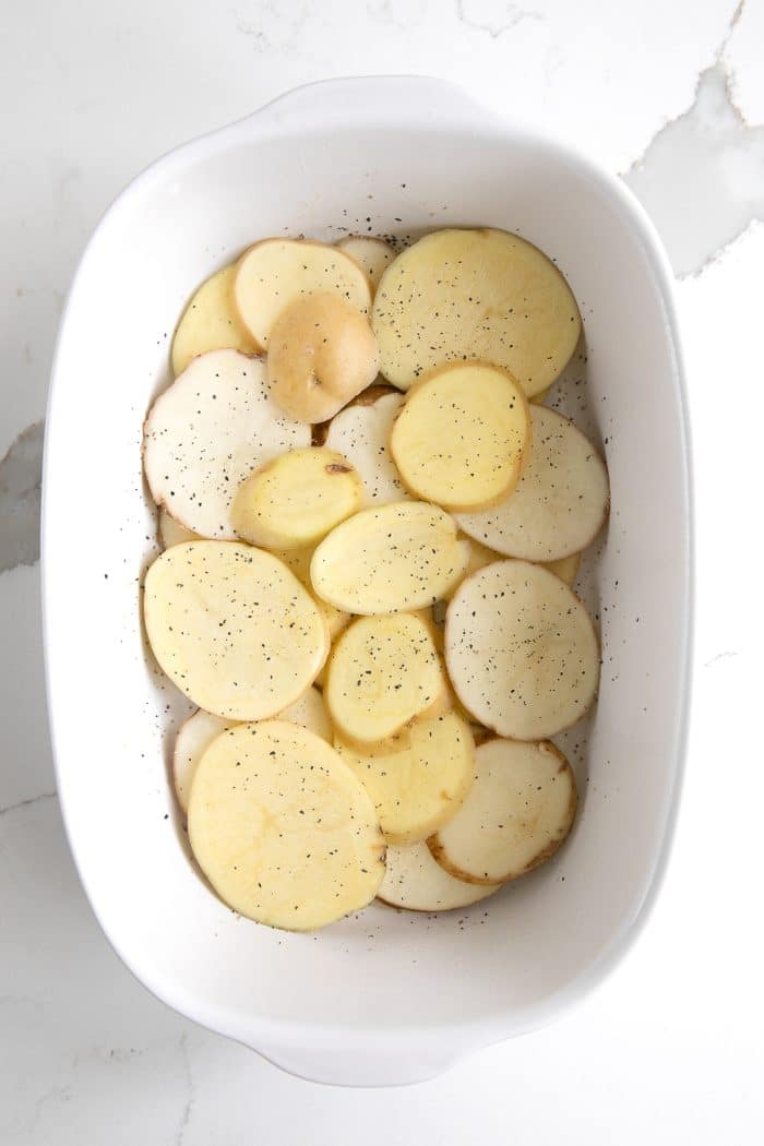 Thinly sliced potatoes in a single layer in a white casserole dish
