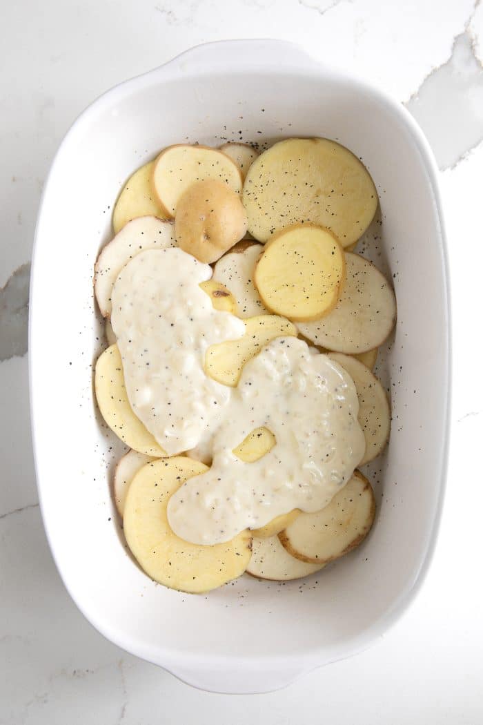 Thinly sliced potatoes in a white casserole dish topped with homemade cream sauce.