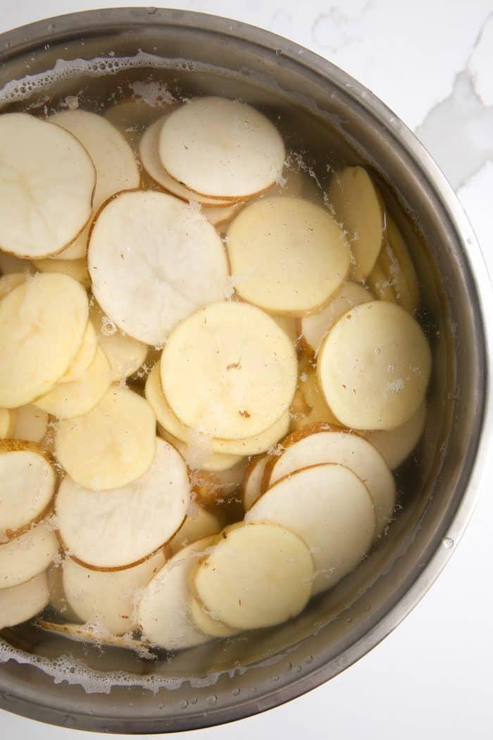 Large bowl filled with thinly sliced potatoes.
