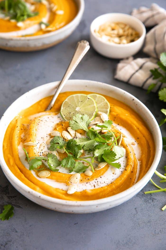White bowl filled with healthy curried pumpkin soup and garnished with coconut milk, lime wheels, and cilantro.