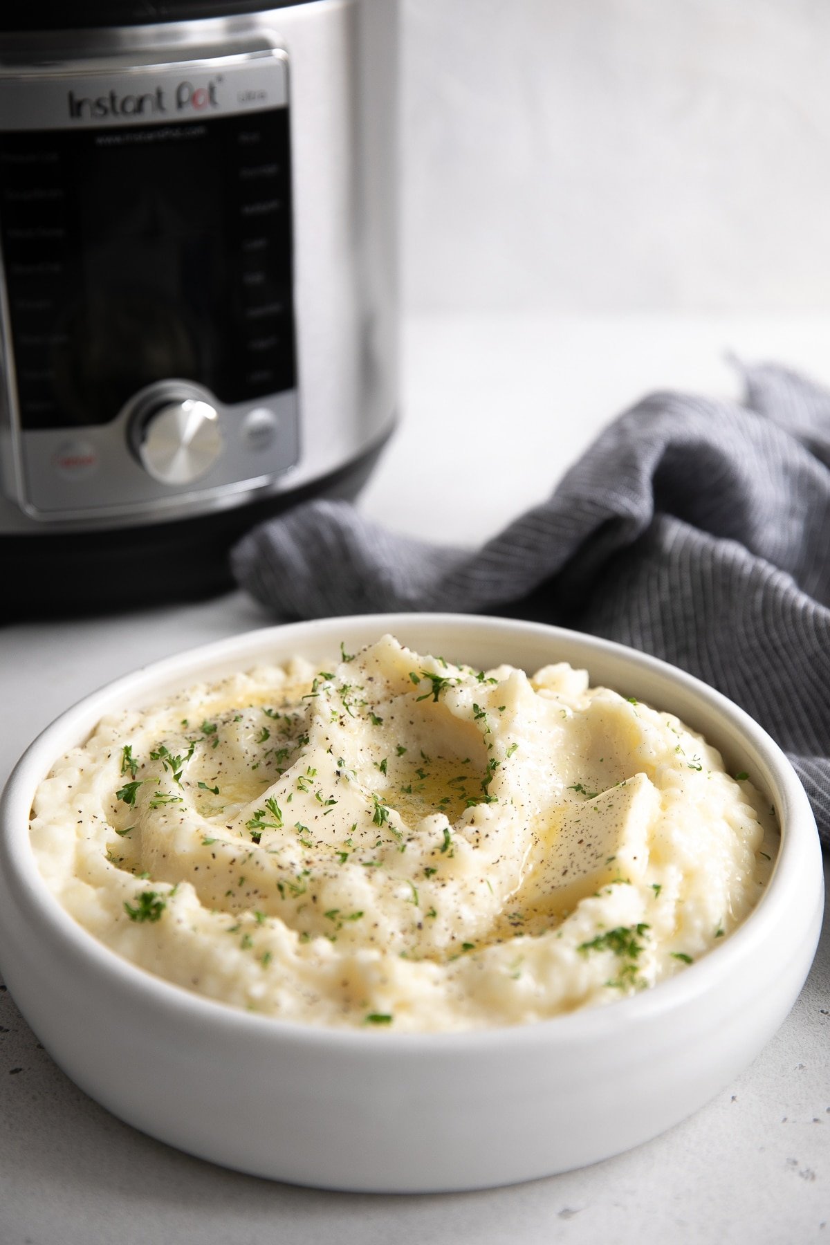 White bowl filled with creamy mashed potatoes and topped with melted butter and finely chopped parsley.