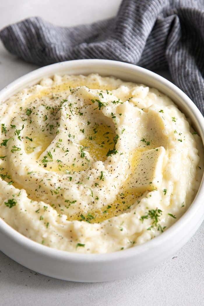 White bowl filled with creamy mashed potatoes and topped with melted butter and finely chopped parsley.