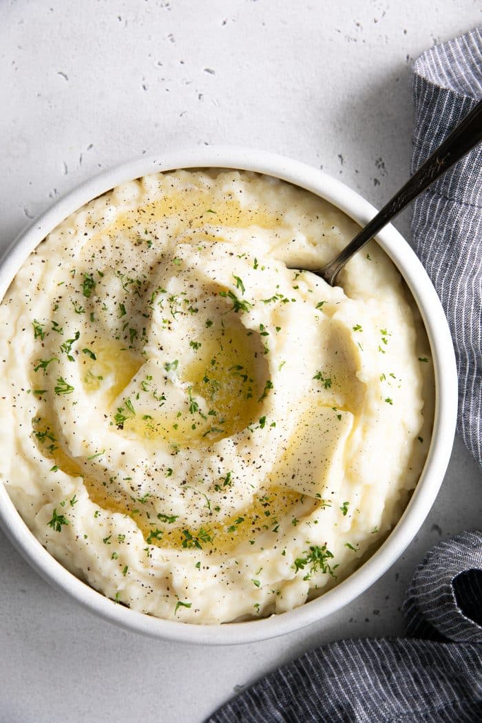 White bowl filled with creamy mashed potatoes and topped with melted butter and finely chopped parsley.