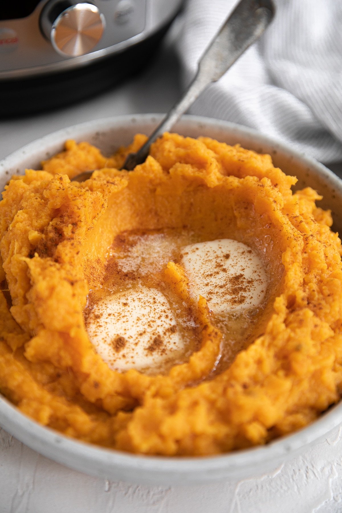 Mashed sweet potatoes cooked in an Instant Pot served in a round, shallow bowl and topped with extra butter.