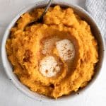 Mashed sweet potatoes cooked in an Instant Pot served in a round, shallow bowl and topped with extra butter.