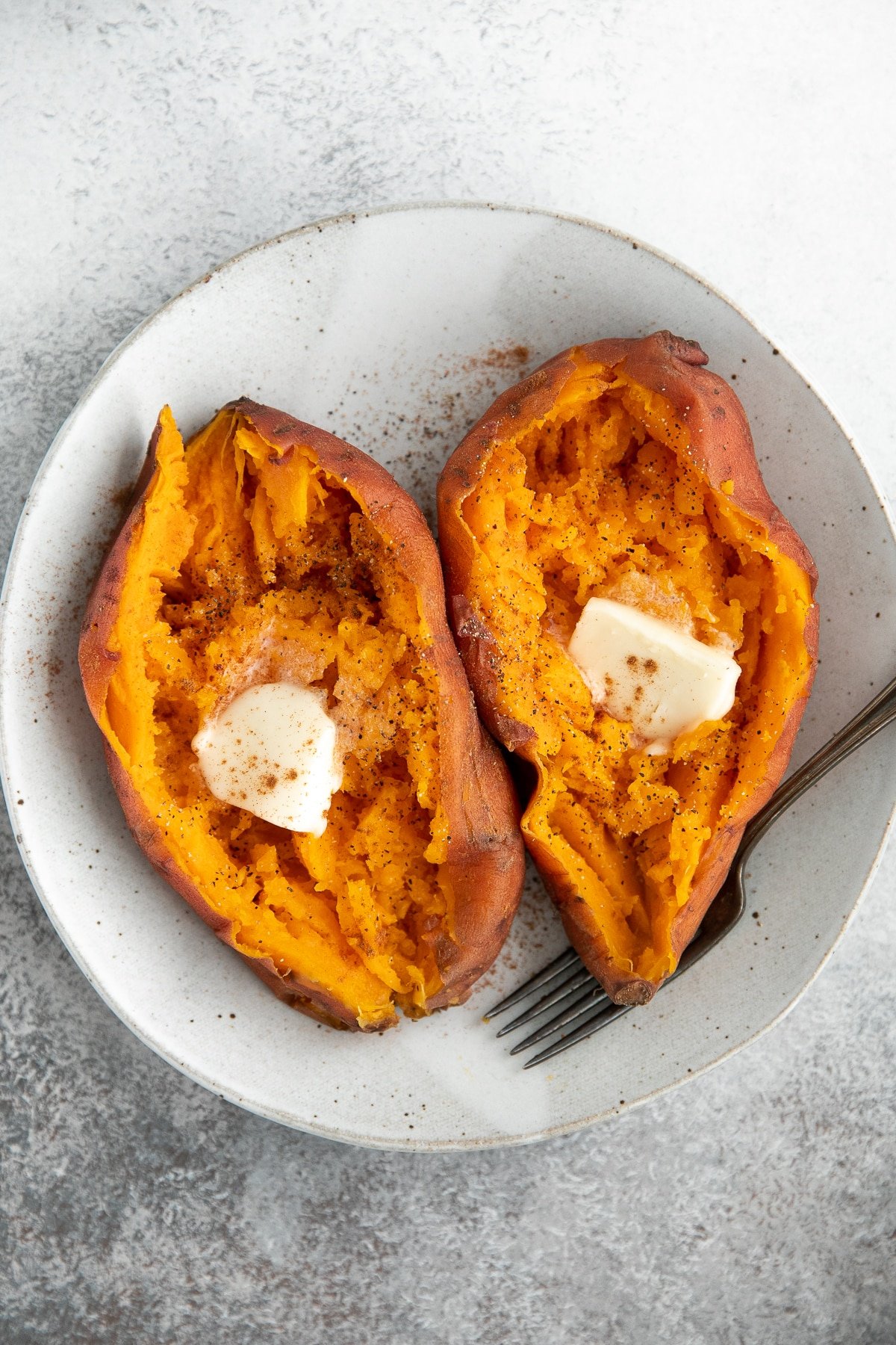 Two cooked sweet potatoes topped with butter.