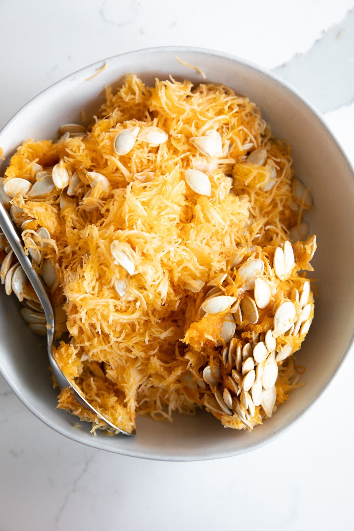 Seeds and guts from the inside of a pumpkin scooped out and removed to a shallow bowl.