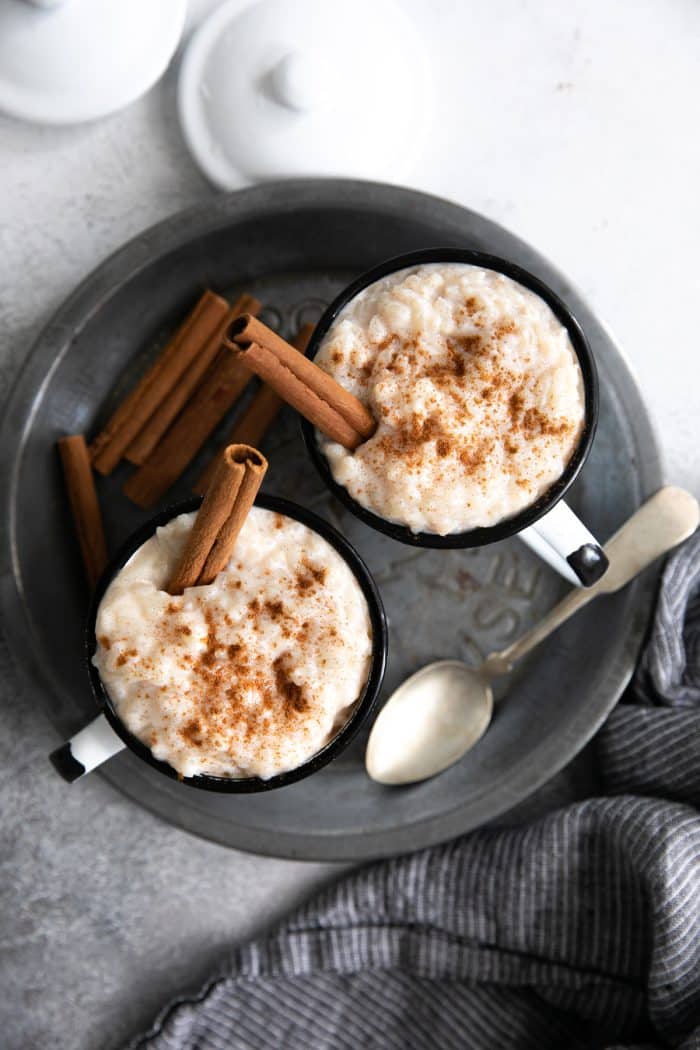 Two mugs filled with creamy Mexican rice pudding sprinkled with ground cinnamon and garnished with a whole cinnamon stick.