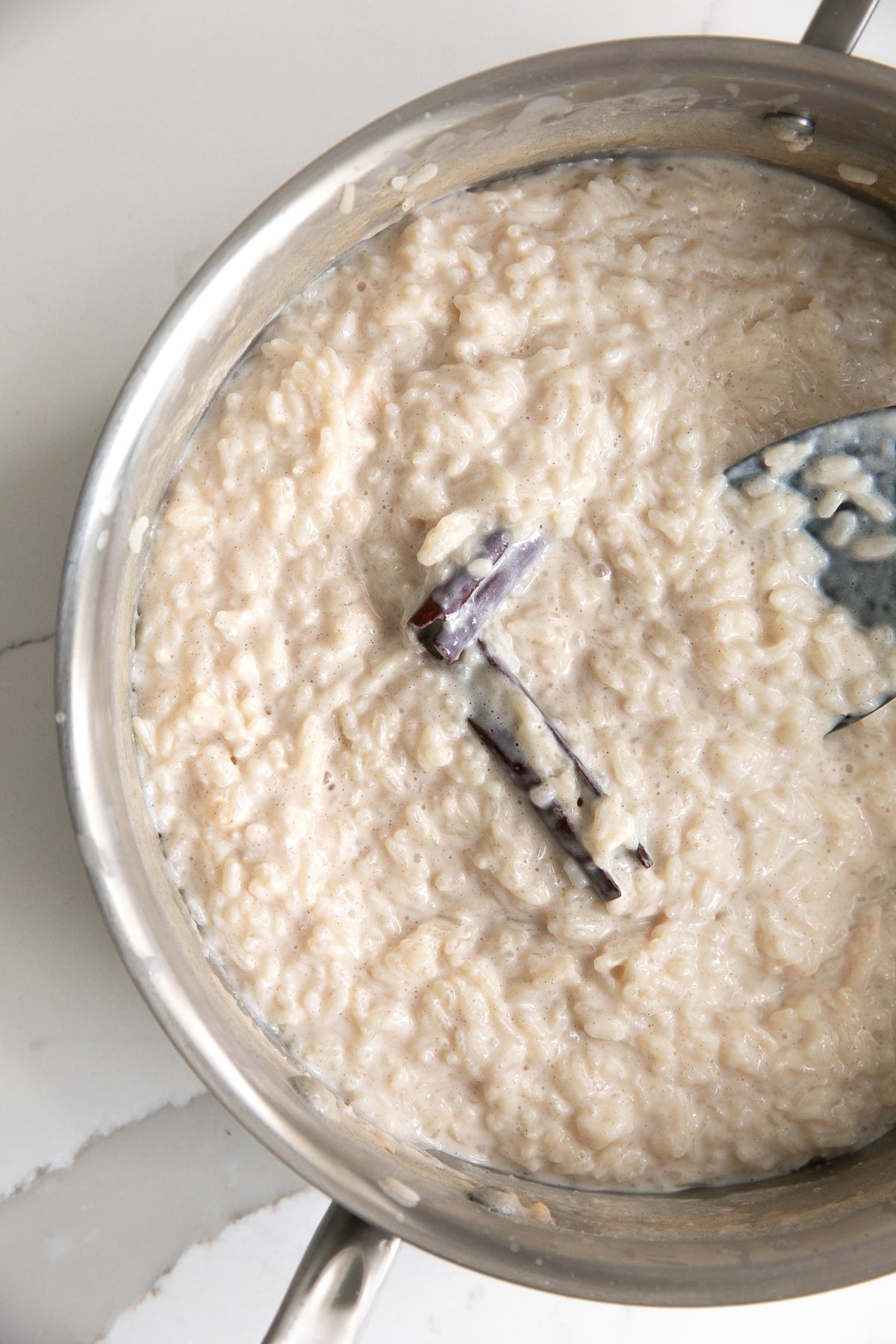 Pot filled with rice simmering in milk and sugar with cinnamon sticks.