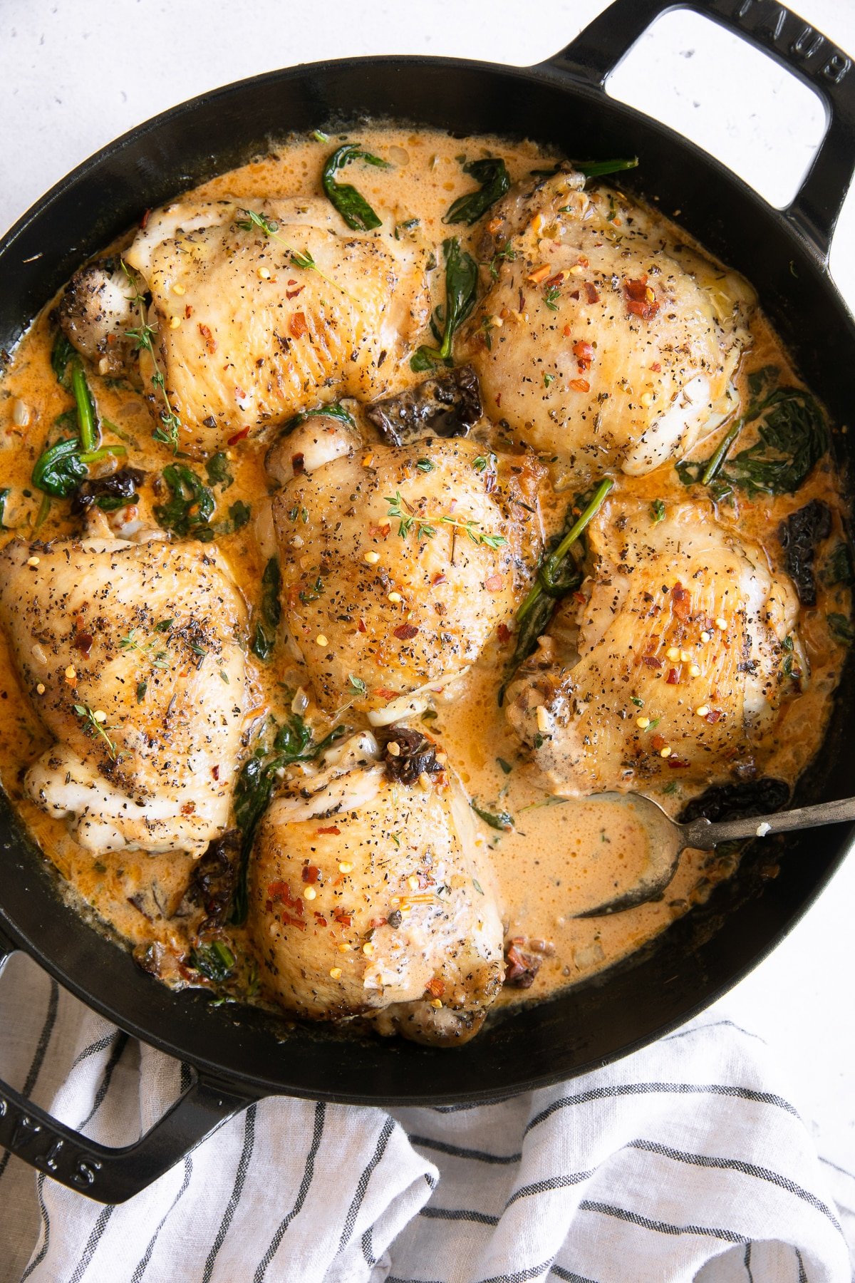 Overhead image of a large skillet filled with 6 cooked chicken thighs in a creamy tuscan sauce with sundried tomatoes and spinach.