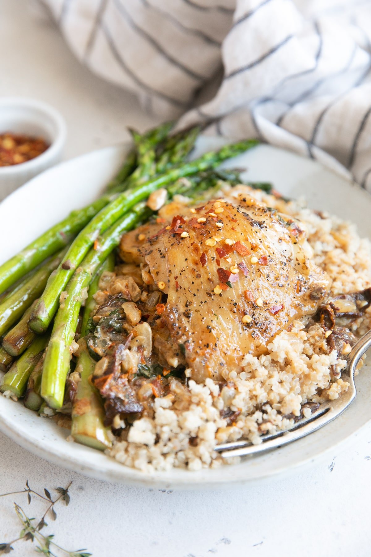 Plate filled with asparagus and quinoa topped with creamy Tuscan chicken.