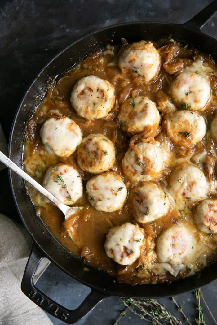 Large skillet filled with turkey meatballs simmering in a rich gravy filled with onions and covered with cheese.