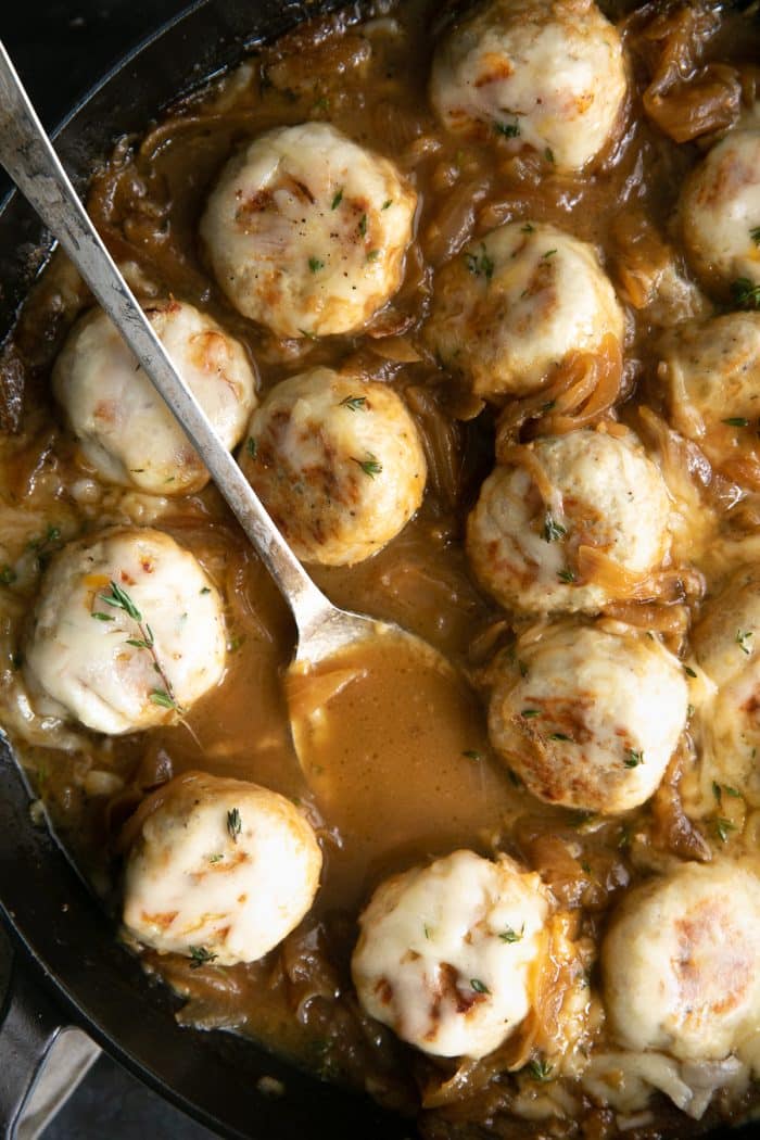 Large skillet filled with turkey meatballs simmering in a rich gravy filled with onions and covered with cheese.