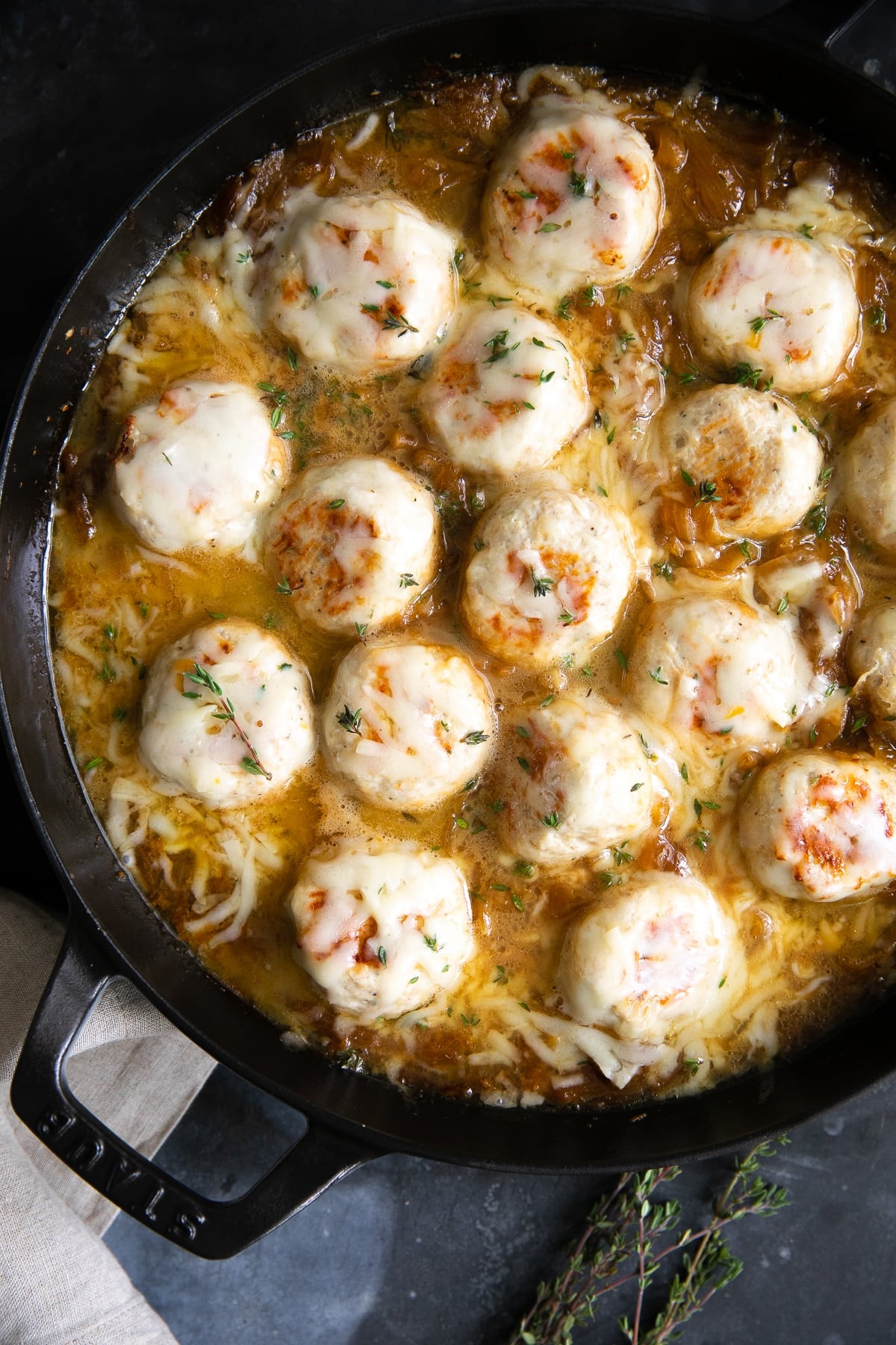 Large skillet filled with turkey meatballs simmering in a rich gravy filled with onions and covered with cheese.
