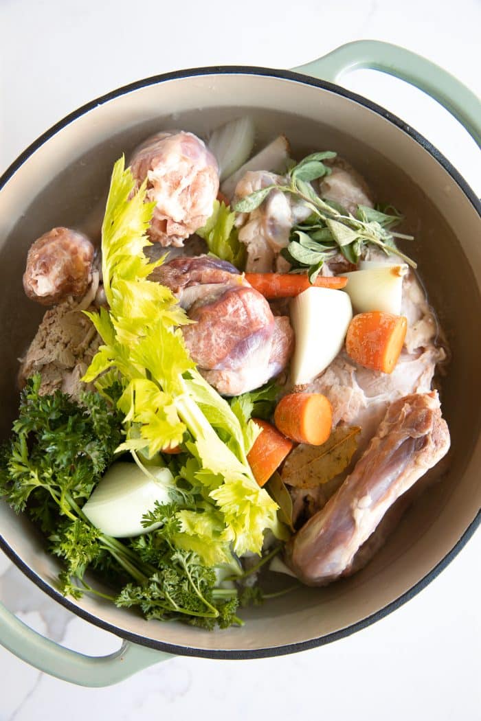 Large Dutch oven filled with leftover turkey carcass, turkey neck and giblets, celery, onion, fresh herbs, and water to make homemade stock that will be used to make turkey soup.