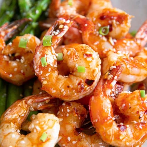Juicy large shrimp simmered in a homemade sauce made with soy sauce, Sriracha, honey, and rice wine vinegar, and garnished with green onions and sesame seeds.