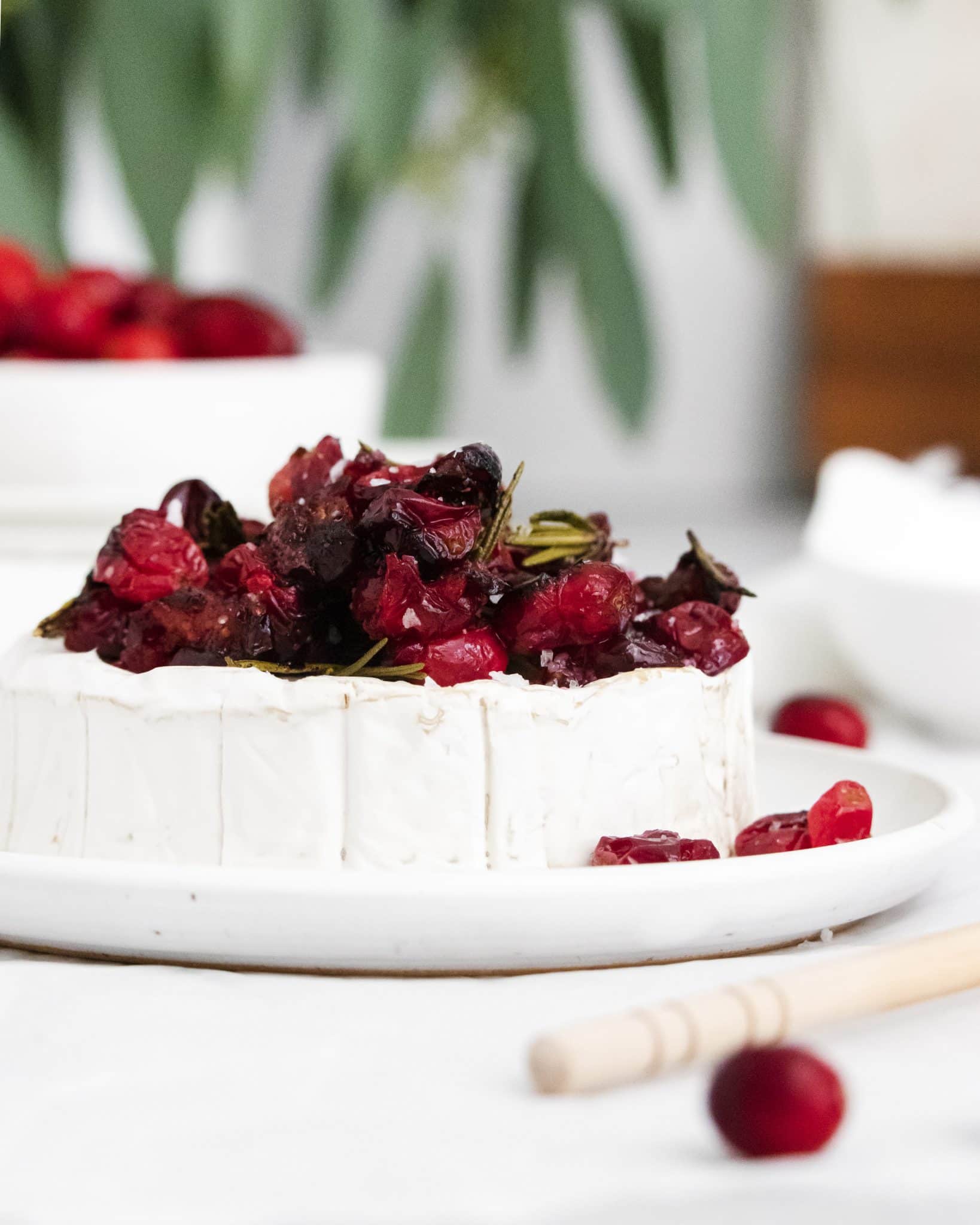 Wheel of brie topped with roasted cranberries and rosemary before being baked.
