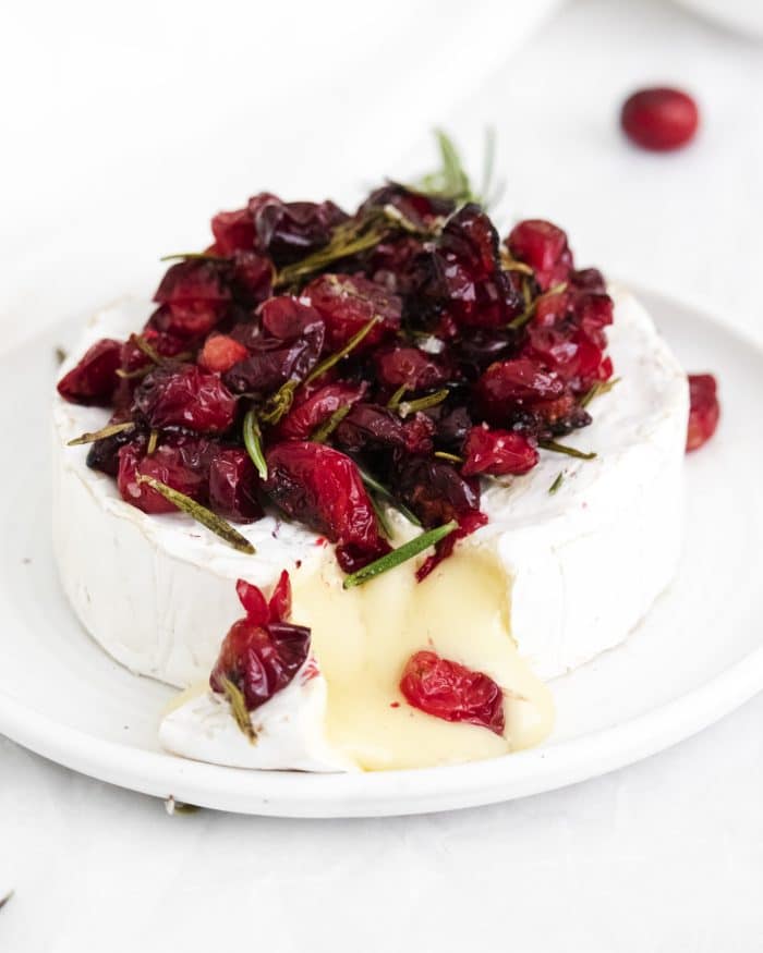 Warm baked brie topped with roasted cranberries cut open to reveal gooey, delicious cheese pouring out.