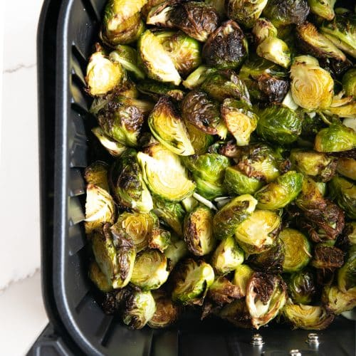 Image of fully cooked and crispy Brussels sprouts resting in the air fryer basket.