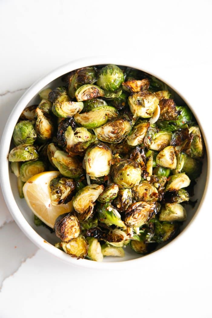 Image of a white serving dish filled with Brussels sprouts cooked in the air fryer and drizzled with a tangy balsamic reduction.