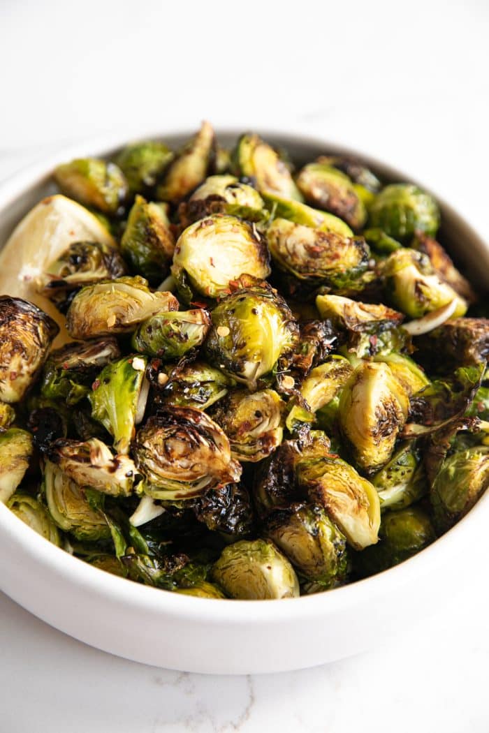 Image of a white serving dish filled with Brussels sprouts cooked in the air fryer and drizzled with a tangy balsamic reduction.