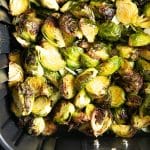 Brussels sprouts roasting in a black air fryer basket, developing golden, crispy edges and a delicious caramelized exterior.