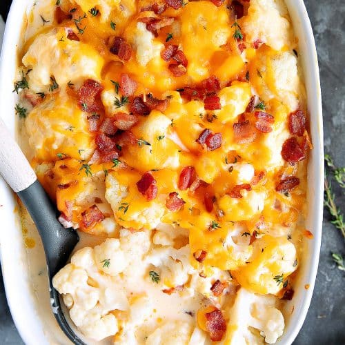 Large with casserole dish filled with cauliflower florets in a homemade cheese sauce and topped with melted cheese and bacon bits.