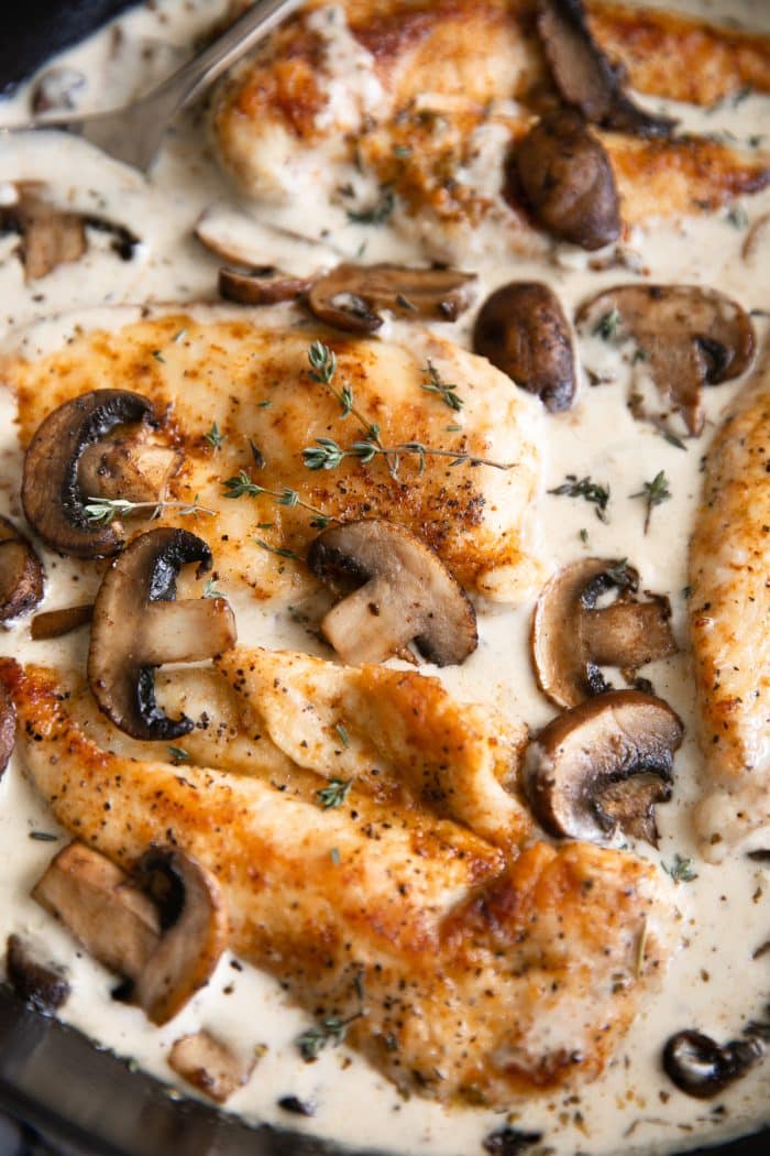 Large heavy-bottomed skillet filled with cooked chicken cutlets simmering in a homemade mushroom cream sauce.