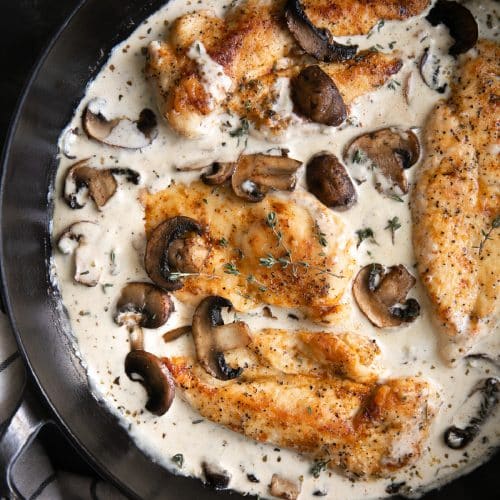 Large cast iron skillet filled with pan-fried chicken cutlets in a creamy mushroom and garlic sauce.