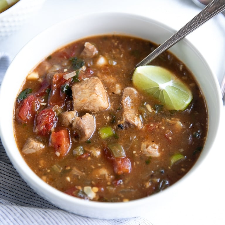 A bowl of instant pot pork green chili stew filled with tender chunks of pork with a lime wedge sinking into the broth.