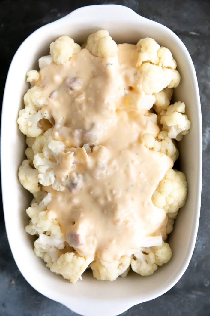 White baking dish filled with blanched cauliflower florets covered in a homemade cheese sauce with bacon.