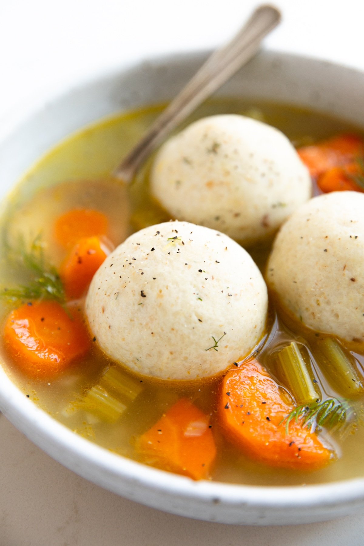 Shallow soup bowl filled with three matzo balls in a vegetable soup.