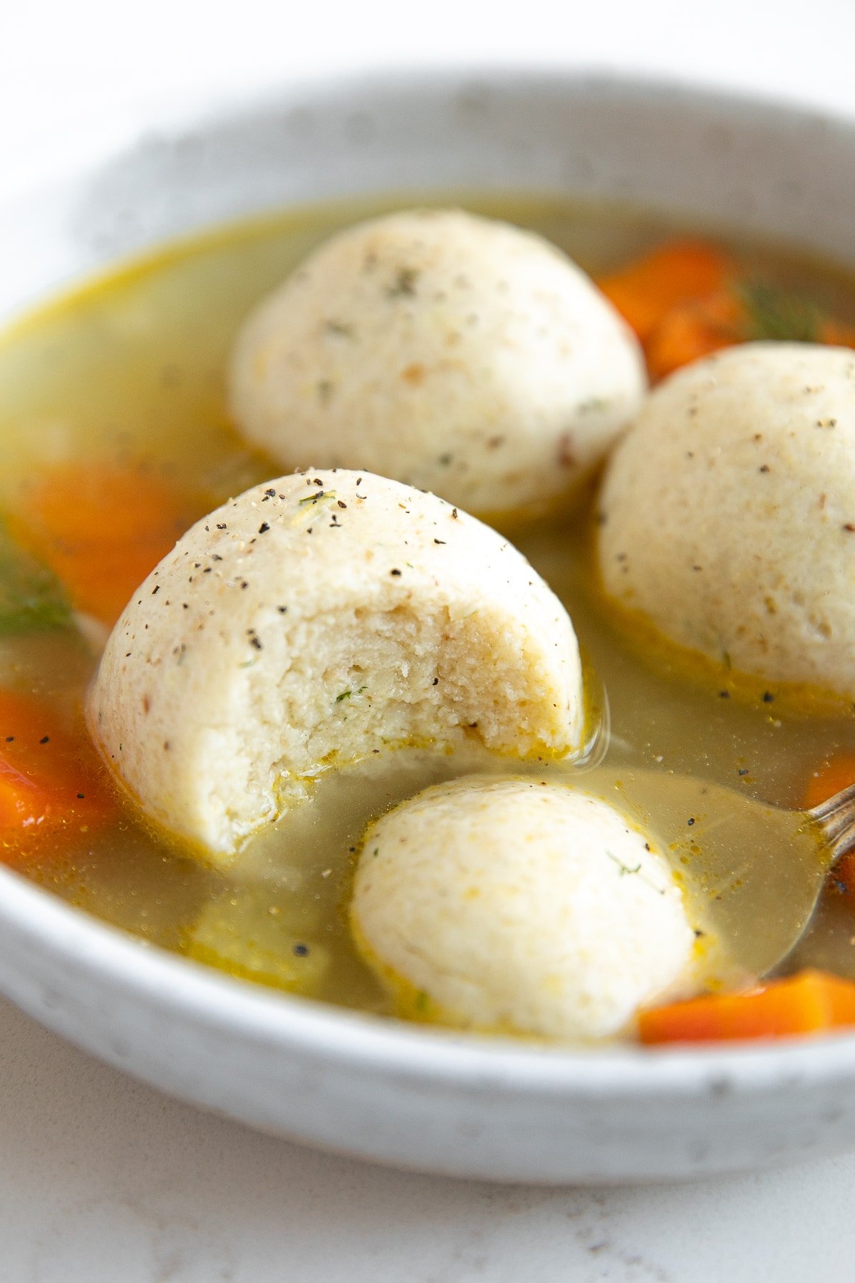 Shallow soup bowl filled with three matzo balls in a vegetable soup.