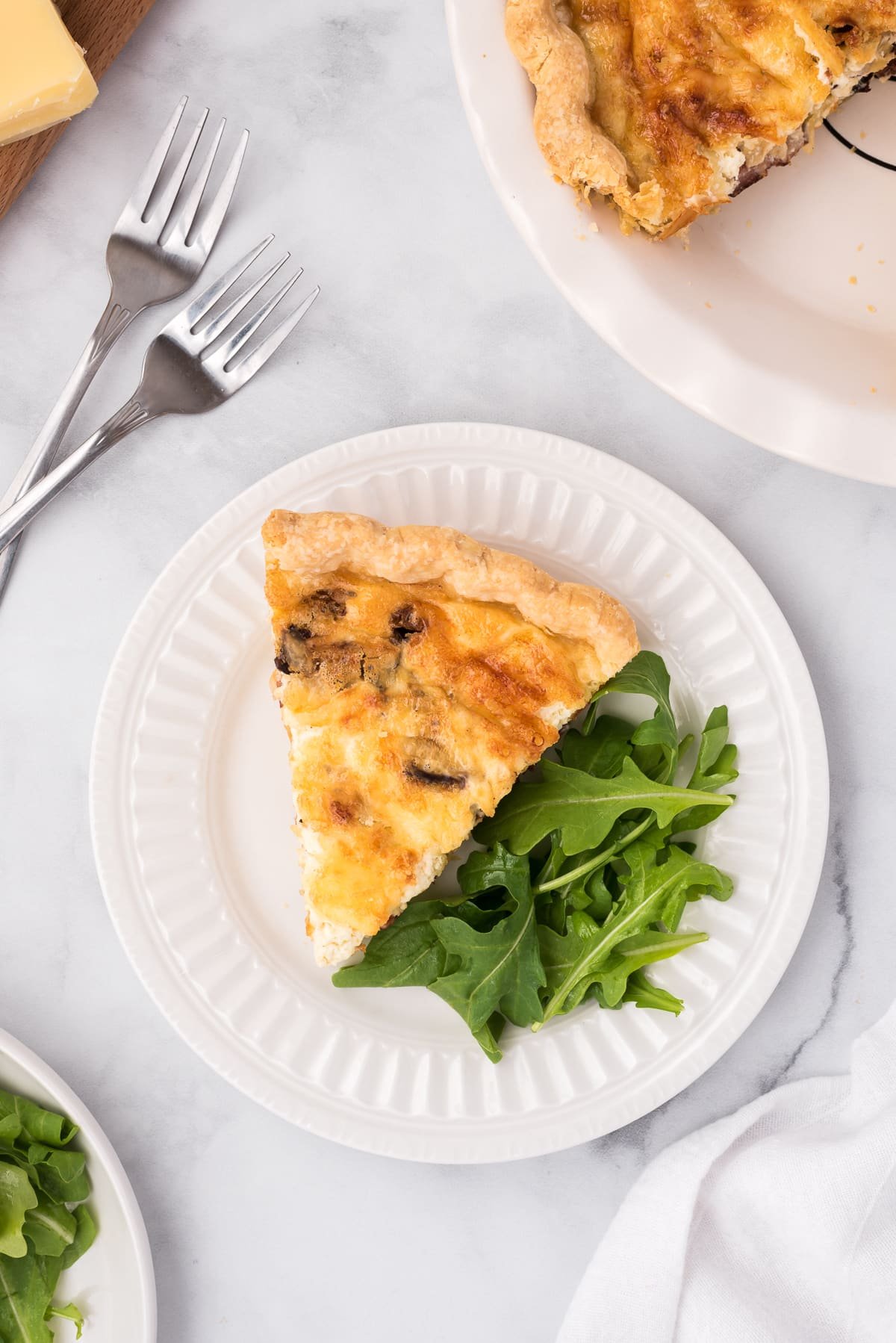 Slice of quiche served with a side of fresh greens on a white serving plate.