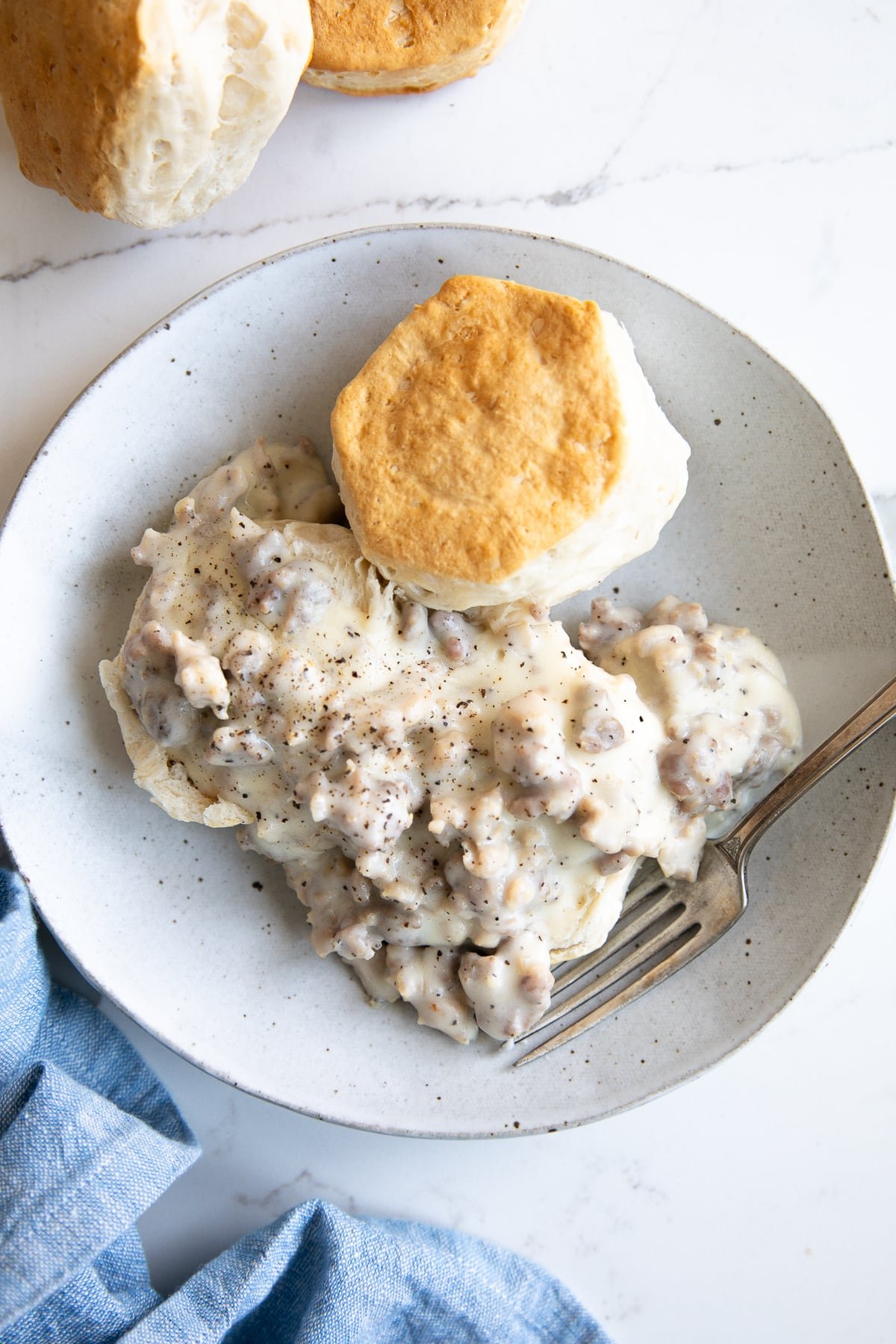 White plate with a fluffy buttermilk biscuit topped with creamy sausage gravy.