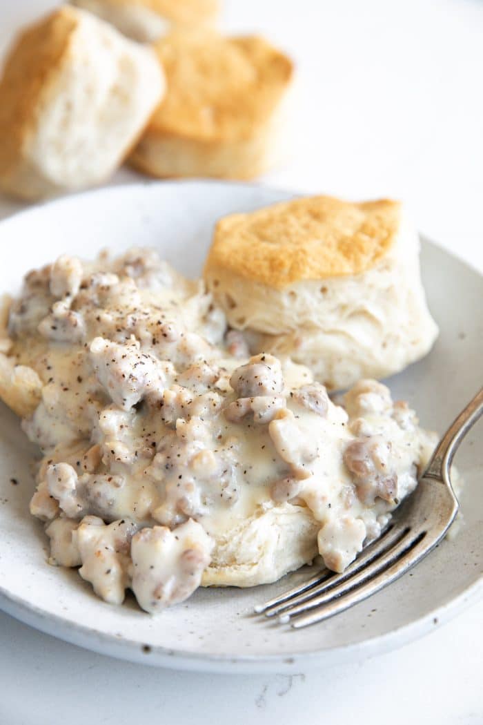 White plate with a fluffy buttermilk biscuit topped with creamy sausage gravy.