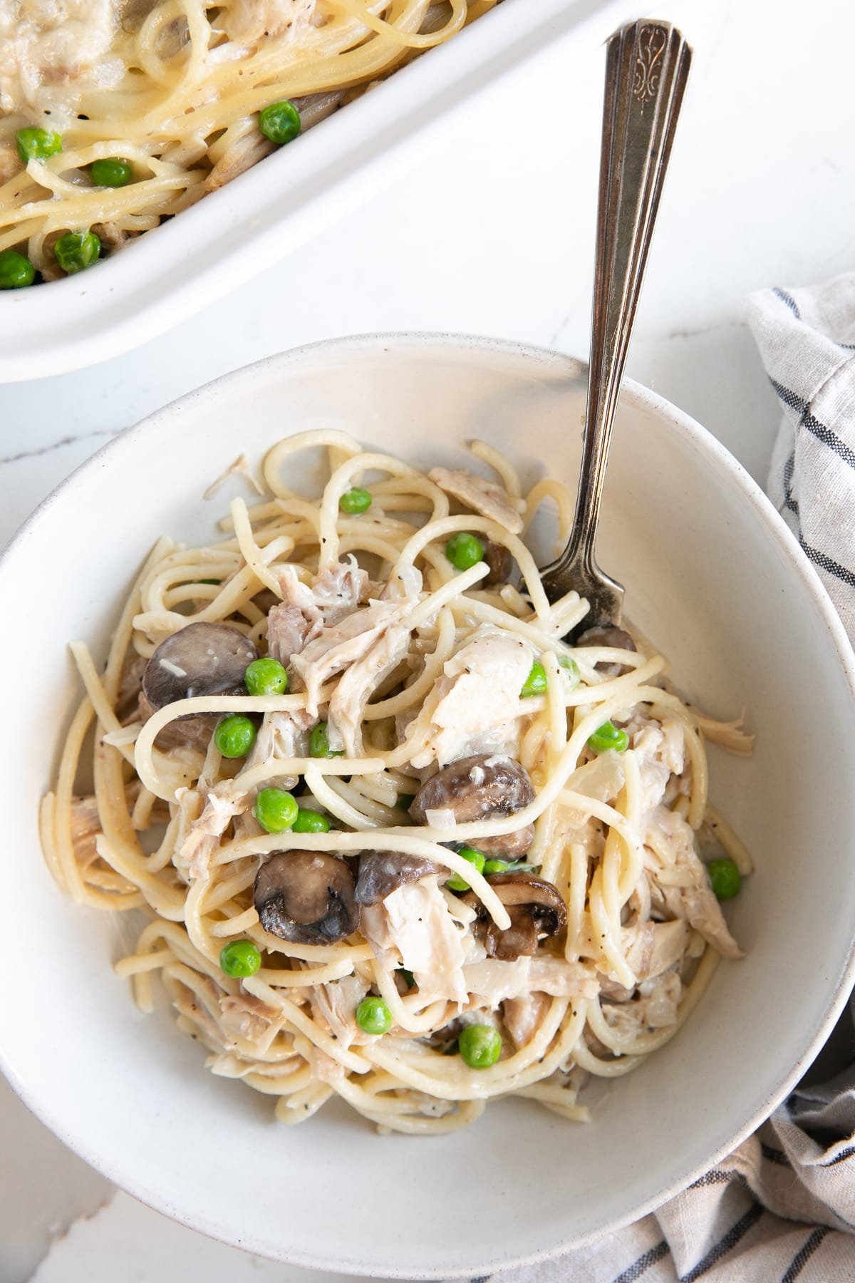 White bowl filled with creamy turkey tetrazzini with peas, mushrooms, and chunks of turkey.
