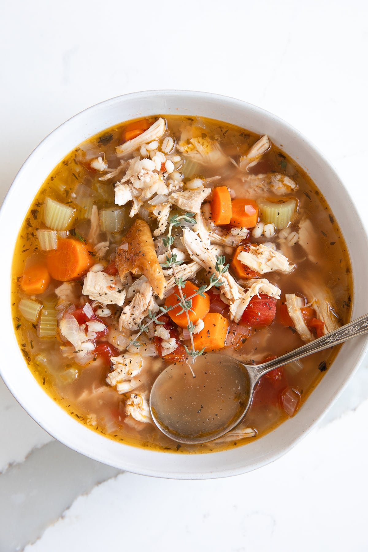 White shallow soup bowl filled with easy turkey soup filled with veggies, tomatoes, turkey, and barley.