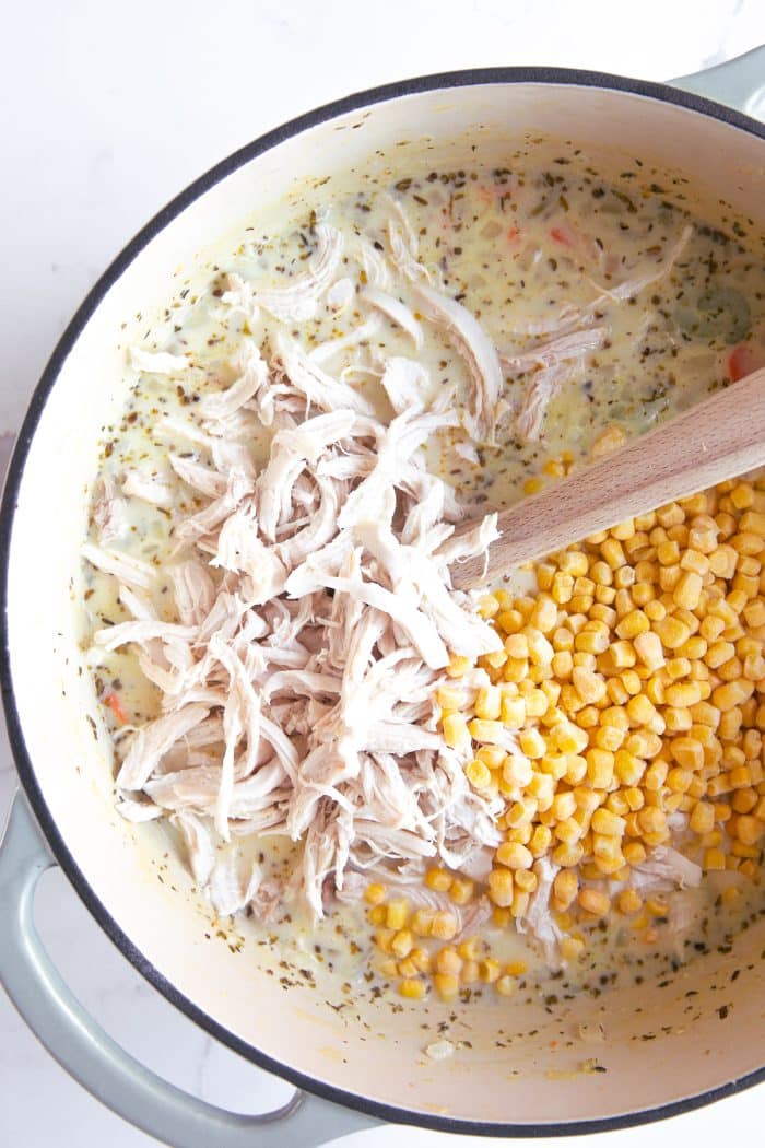 Image of a large Dutch oven filled with a cream-based soup with shredded chicken and frozen corn.