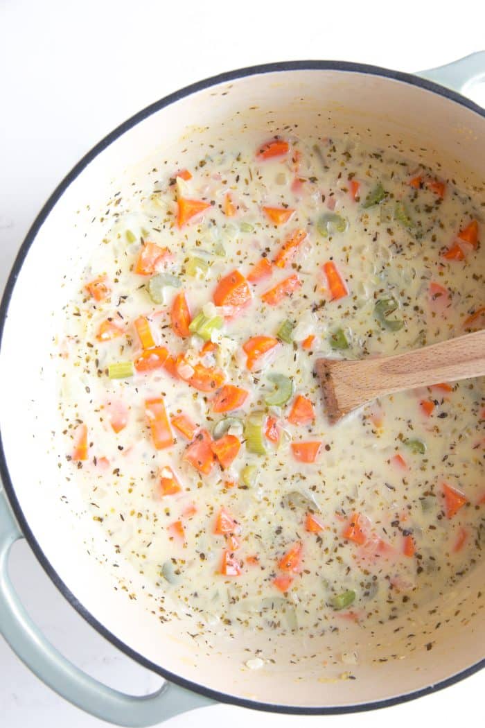 Simmering creamy soup base with carrots and celery in a Dutch oven, seasoned with herbs.