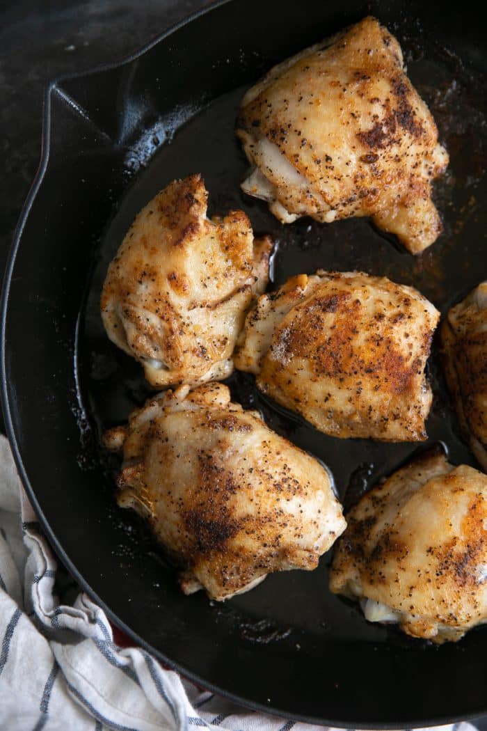 Overhead image of six cooked chicken thighs in a large enameled skillet.