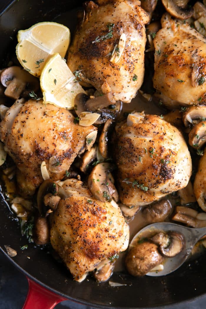 Overhead image of cooked chicken thighs in a light mushroom garlic sauce in a large skillet.